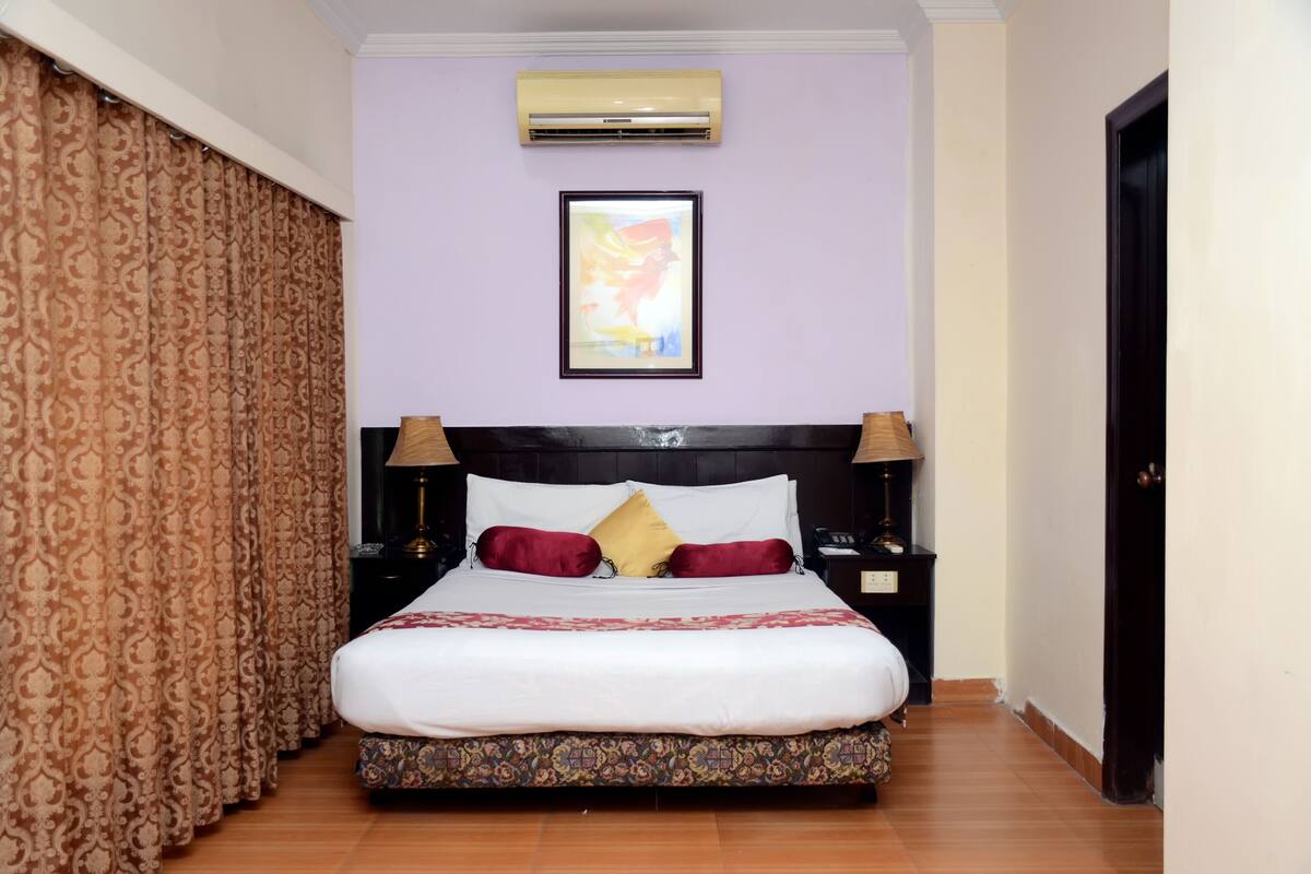 A neatly made bed with a patterned bedspread, two bedside tables with lamps, a framed picture on the wall, and a door to the right.