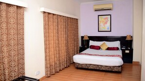 A hotel room with a large bed, patterned curtains, an air conditioning unit, and a framed picture on the wall. - Mirage Hotel (Lahore)