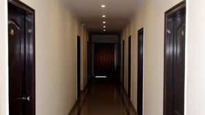 A long, narrow hallway with dark wooden doors on both sides, leading to a room with a red curtain. - Mirage Hotel (Lahore)