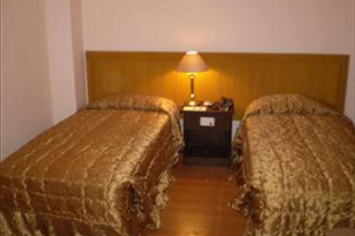 A room with two beds, a nightstand with a lamp, and a wooden headboard.