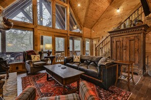 A spacious room with a large window, a fireplace, a leather sofa, and a wooden cabinet.