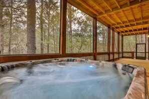 A hot tub in a wooden cabin with large windows overlooking a forest.
