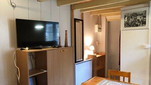 Una mesa de comedor de madera con un mantel individual, un televisor sobre un mueble de madera, una lámpara y un cuadro enmarcado en la pared.