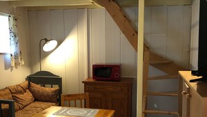 Una habitación acogedora con una mesa de madera, un microondas rojo, un armario de madera, una silla y una escalera.