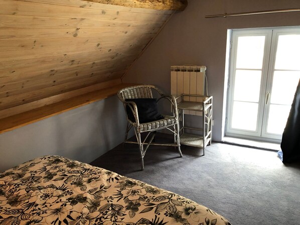 A room with a sloped ceiling, a wicker chair, a bed with a floral bedspread, and a window with a view.