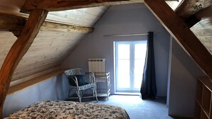 Un dormitorio con techo inclinado, una cama con colcha floral, una silla, un radiador y una ventana con cortina.