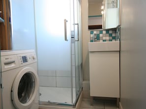 Modern bathroom with washing machine, glass-enclosed shower, and storage cabinet.