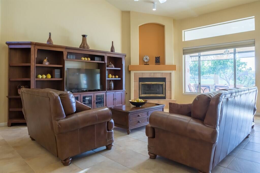 A living room with a fireplace, leather sofas, a TV, and a bookshelf.