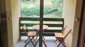 A balcony with two wooden chairs and a small round table, overlooking a grassy area with trees and a stone wall. - T2 Bis Apartment for 6 People with Parking in Cauterets (Cauterets)