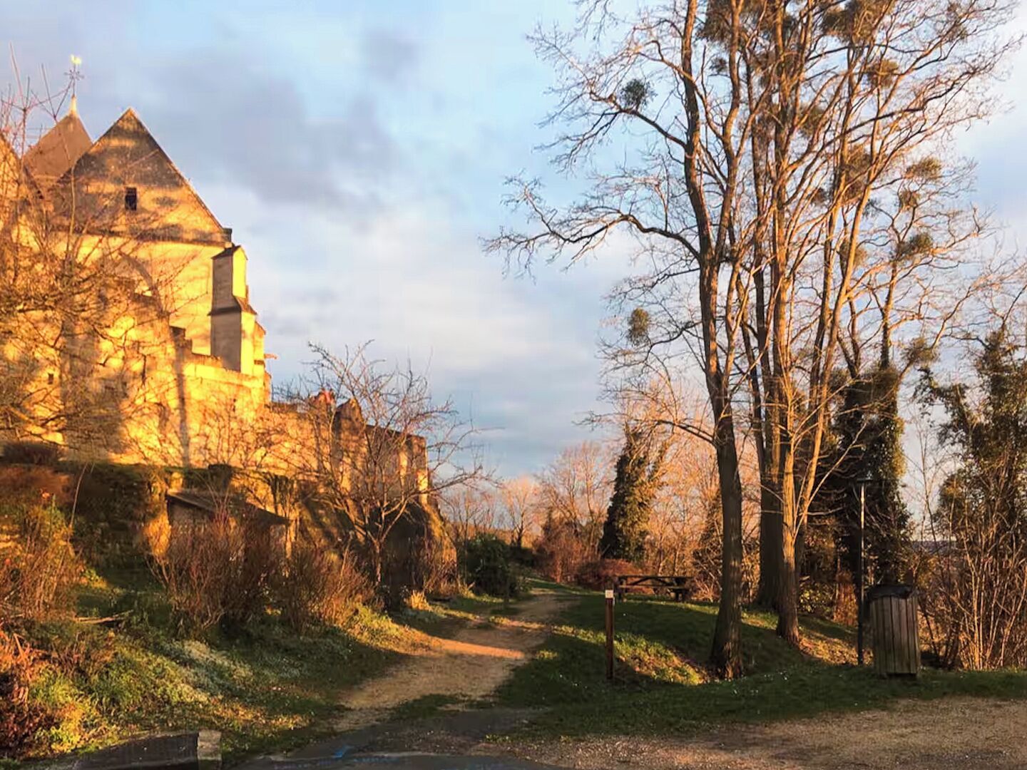Un bâtiment historique doté d’une tour imposante, entouré d’arbres et accessible par un sentier.