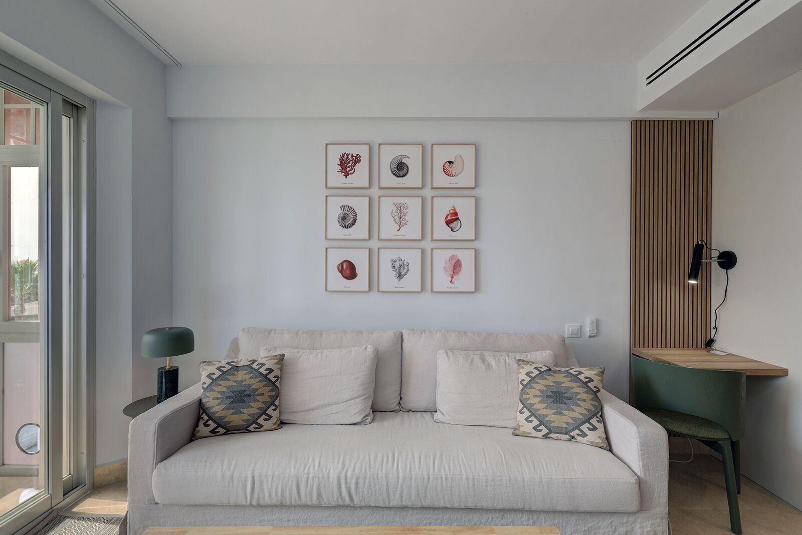 Una sala de estar moderna con un sofá, almohadones decorativos, una lámpara de pared y obras de arte enmarcadas.