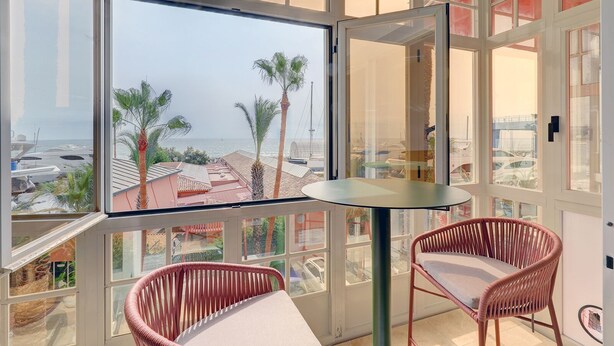 A balcony with a glass door, two wicker chairs, and a round table. - Ale Maison sotogrande port and beachfront private terrace sea view (San Roque)