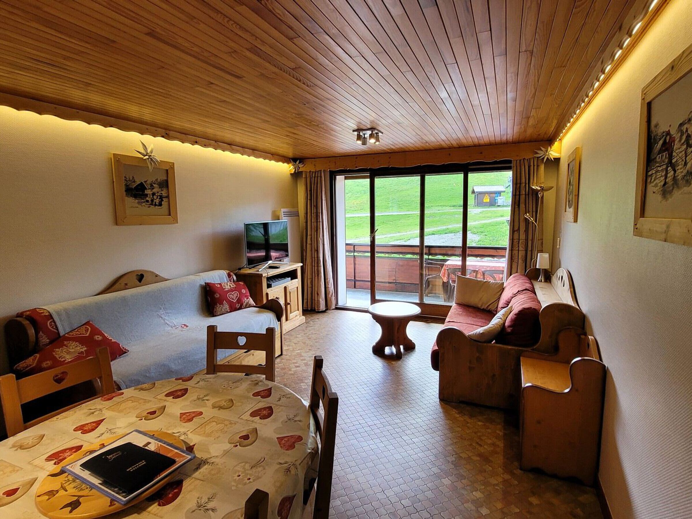 Una stanza accogliente con soffitto in legno, televisore, tavolo da pranzo con un libro e divano.