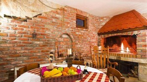 Una habitación rústica con paredes de ladrillo visto, una chimenea de ladrillo y una mesa redonda con cesta de fruta.