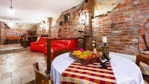 Un área de comedor con pared de ladrillo, sofá de cuero rojo y una mesa con mantel a cuadros y frutera.