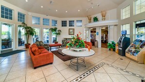A spacious lobby with a central round table, multiple seating areas, and a view of the outside through large windows. - Magic Escape- Themed Bedrooms, Pool/Spa, Game Room, Movie Theater! Near Disney! (Kissimmee)