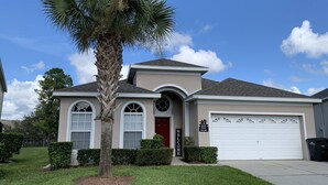 A single-story house with a red door, a garage, and a palm tree in the front yard. - Magic Escape- Themed Bedrooms, Pool/Spa, Game Room, Movie Theater! Near Disney! (Kissimmee)