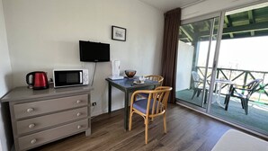 Una habitación con escritorio de madera, televisor, microondas, tetera y una mesa de comedor con sillas.