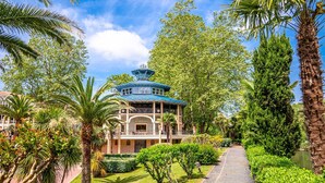Un edificio de estilo tradicional con techo azul, rodeado de exuberante vegetación y palmeras.