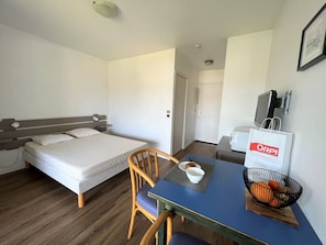 Quarto de hotel com uma cama, uma mesa com uma tigela de frutas, uma cadeira e uma televisão.