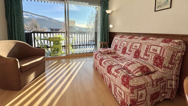 A cozy living room with a sofa and a chair, a balcony with a view of a snowy landscape, and a framed picture on the wall. - Perfect ski studio, balcony, parking - Notre-Dame-de-Bellecombe (Notre-Dame-de-Bellecombe)