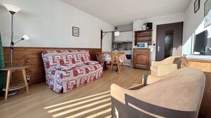 A cozy living room with a patterned sofa, a wooden dining table, and a kitchen area with a microwave. - Perfect ski studio, balcony, parking - Notre-Dame-de-Bellecombe (Notre-Dame-de-Bellecombe)