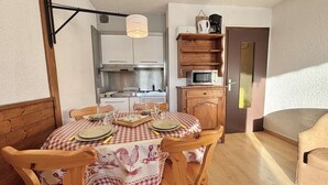 A cozy dining area with a checkered tablecloth, wooden chairs, and a kitchen in the background. - Perfect ski studio, balcony, parking - Notre-Dame-de-Bellecombe (Notre-Dame-de-Bellecombe)