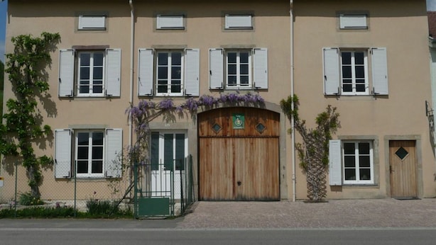 Ein zweistöckiges Gebäude mit roten Ziegeln, weißen Fensterläden und einer Holztür, über der ein grünes Schild angebracht ist.