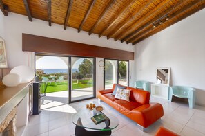 Un salon moderne avec une table basse en verre, un canapé en cuir et une vue sur un paysage verdoyant grâce à de grandes portes coulissantes.