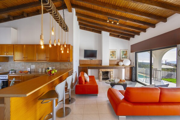A modern kitchen with wooden cabinets, a bar area, and a seating area with orange sofas.