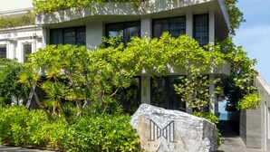 Un bâtiment moderne doté de nombreux balcons ornés de verdure, une enseigne en pierre sur laquelle on peut lire le mot « SUITE », et une zone d’entrée pavée.