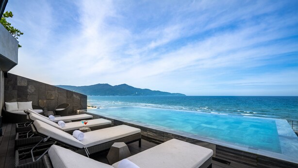 Une piscine à débordement avec des chaises longues et une vue sur l’océan.
