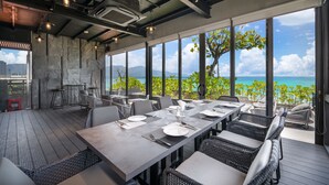 Un restaurant doté d’une longue table dressée pour le dîner, de grandes fenêtres offrant une vue sur l’océan et les montagnes, et d’un plafond au design industriel moderne.