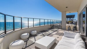 A balcony with a view of the ocean, white outdoor furniture, and a staircase leading to another level.