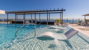 A rooftop infinity pool with clear blue water, a sun terrace with lounge chairs, and a pergola structure. - Spacious Beach Front Balcony | walking distance to ALL local hotspots (Gulf Shores)