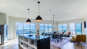 A modern kitchen with a central island, dining area with chairs, and a sofa with a view of the ocean. - Spacious Beach Front Balcony | walking distance to ALL local hotspots (Gulf Shores)