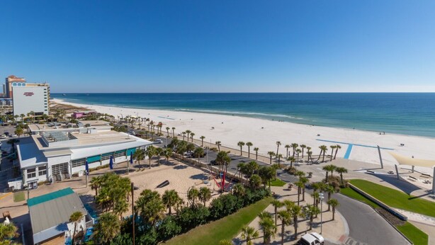 A beachside hotel with a pool, palm trees, and a view of the ocean. - Spacious Beach Front Balcony | walking distance to ALL local hotspots (Gulf Shores)