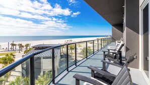 A balcony with a glass railing overlooking a beach. - Spacious Beach Front Balcony | walking distance to ALL local hotspots (Gulf Shores)