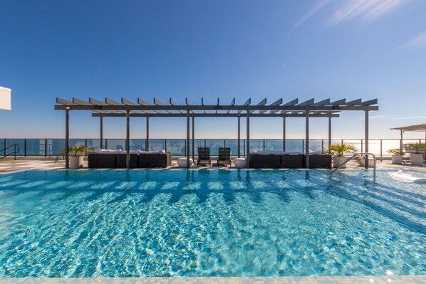 Une piscine à débordement située sur le toit, avec une eau d’un bleu cristallin, entourée de chaises longues et d’une pergola.