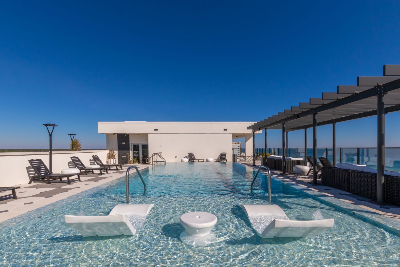 A rooftop infinity pool with lounge chairs and a covered seating area, overlooking the ocean.