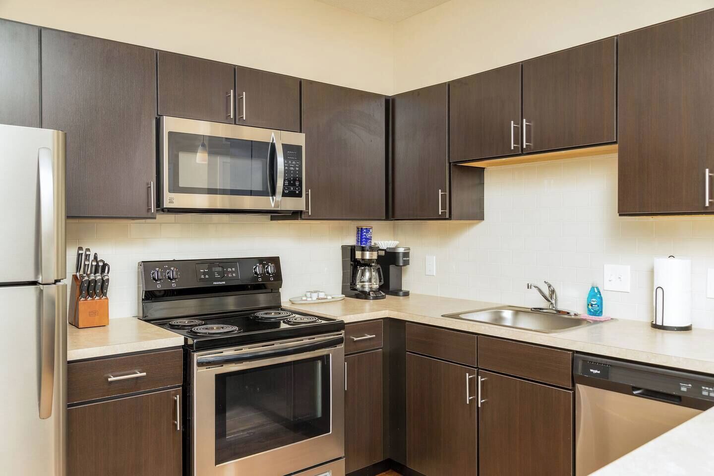 Una cocina moderna con armarios de madera oscura, electrodomésticos de acero inoxidable y encimera blanca.