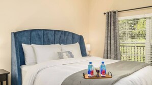 Een hotelkamer met een groot bed, een nachtkastje, een raam met gordijnen en een dienblad met twee waterflessen.