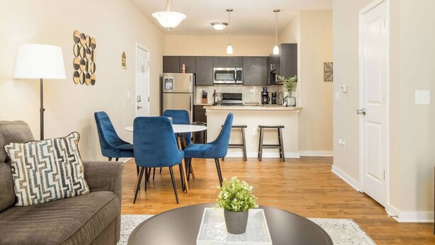 Een moderne woonkamer met een bank, blauwe fauteuils, een salontafel en een keuken op de achtergrond.