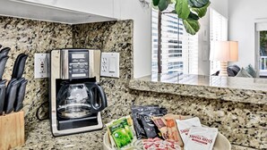 Eine Hotelküche mit Kaffeemaschine, einem Mülleimer mit Essensresten und Blick auf Gebäude durch das Fenster.