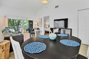 A dining area with a round table, blue placemats, white chairs, and a vase with dried plants.