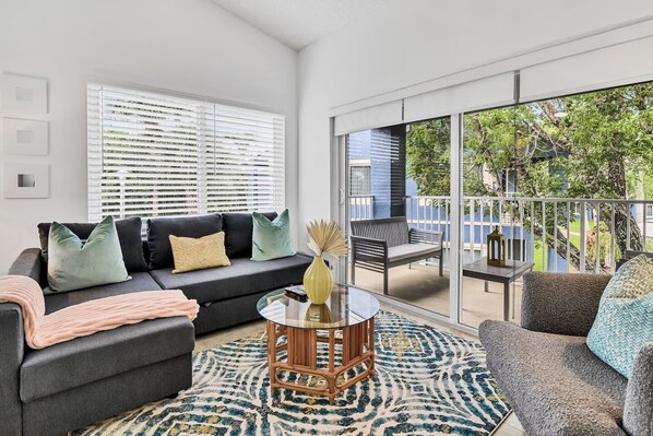 A modern living room with a grey sofa, patterned rug, and a glass coffee table.