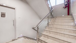 Una escalera con escalones de mármol y barandilla de metal, que conduce a una puerta con un pequeño ventanal.