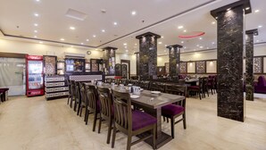Un restaurante con pilares de mármol, mesas de madera y sillas con cojines morados.