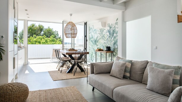 A modern living room with a sofa, a dining table with chairs, and a large window overlooking greenery. - Town house in Silves (Silves)