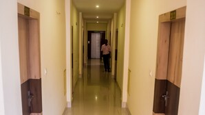 Un pasillo con puertas a ambos lados, una persona caminando a lo lejos y un accesorio de iluminación en el techo.